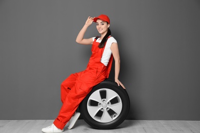 Female mechanic in uniform with car tire on grey wall background