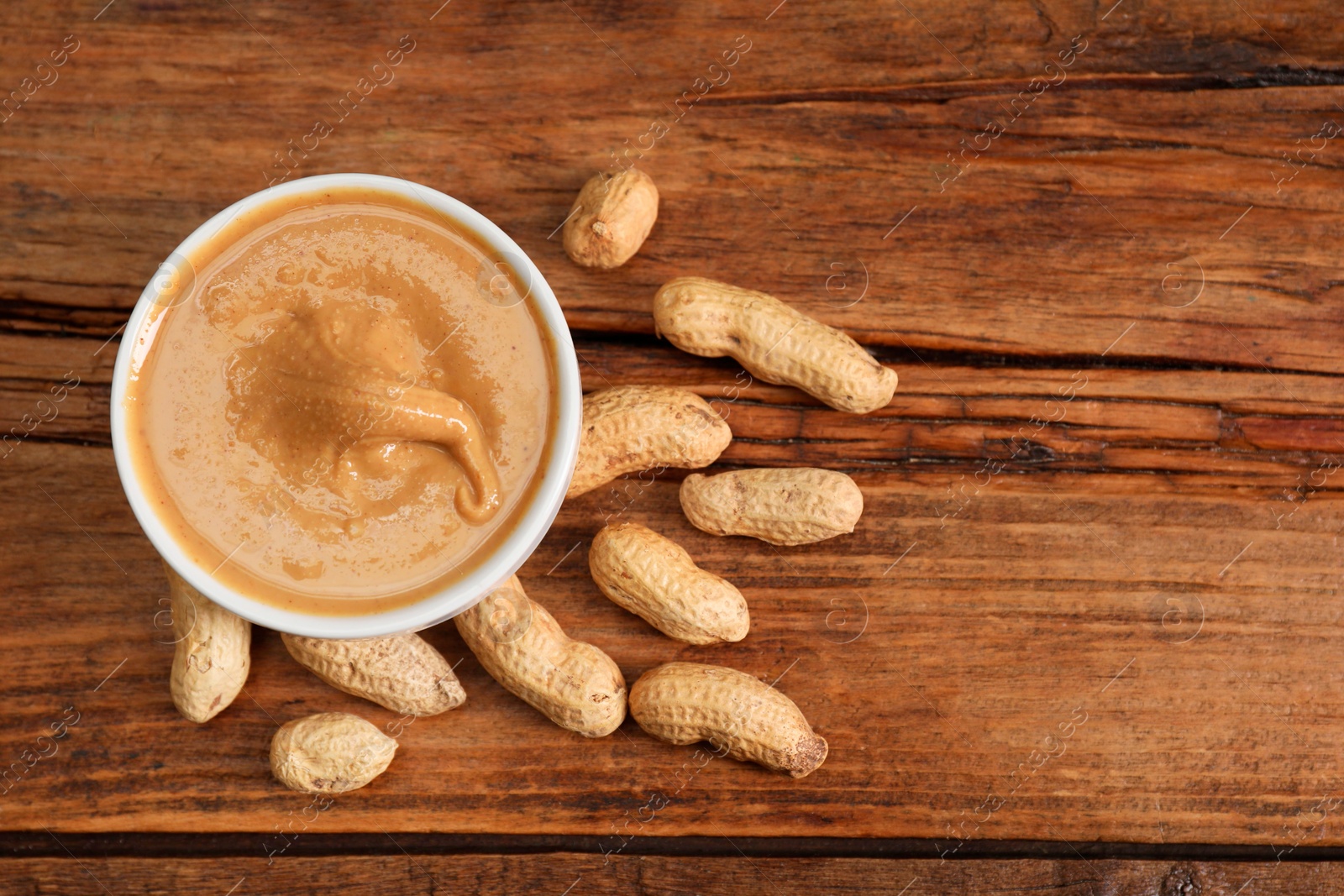 Photo of Delicious nut butter in bowl and peanuts on wooden table, top view