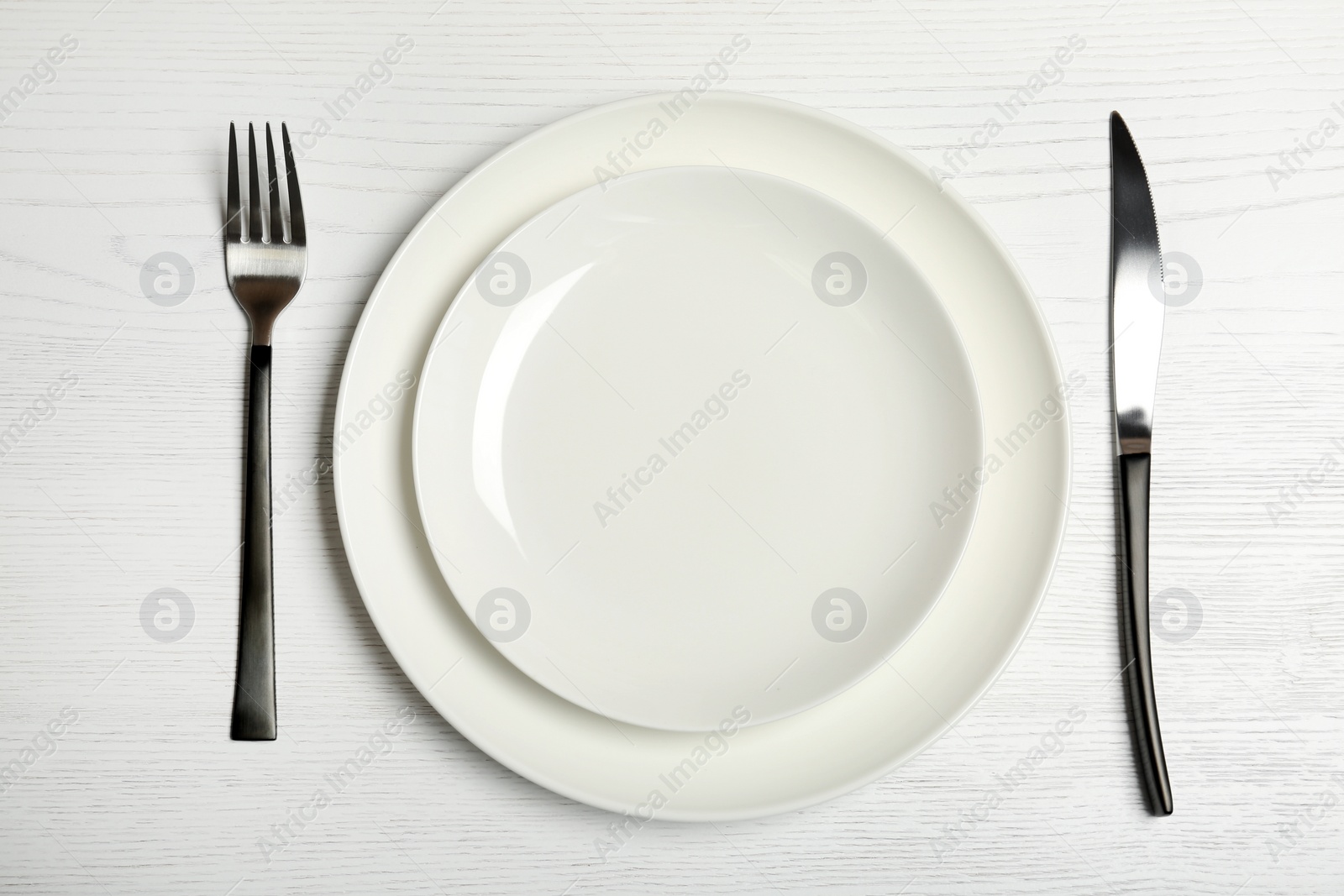 Photo of Plates, fork and knife on wooden table, top view. New setting