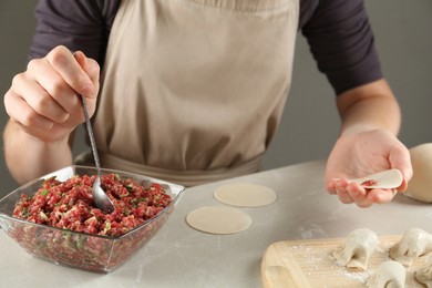 Photo of Woman putting gyoza filling in center of dough wrapper at light table, closeup