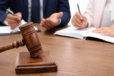 Photo of Wooden gavel and blurred lawyer with client on background