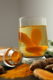 Glass cup of tasty tea, turmeric roots and powder on black textured table