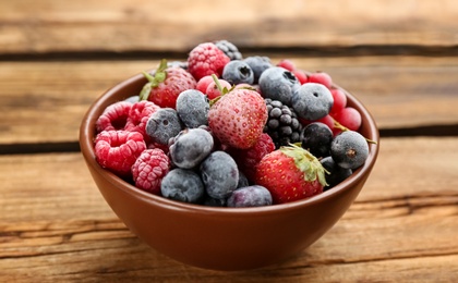 Mix of different frozen berries in bowl on wooden table, closeup