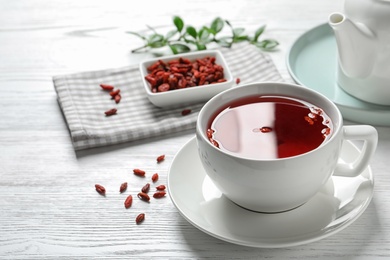 Photo of Healthy goji tea in cup on white wooden table