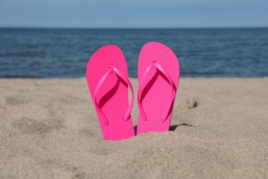 Photo of Stylish pink flip flops on beach sand