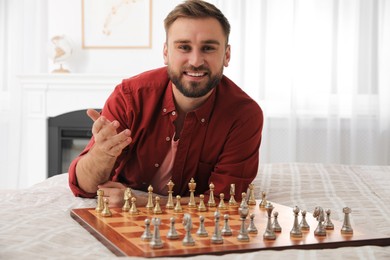 Photo of Happy young man playing chess on bed at home