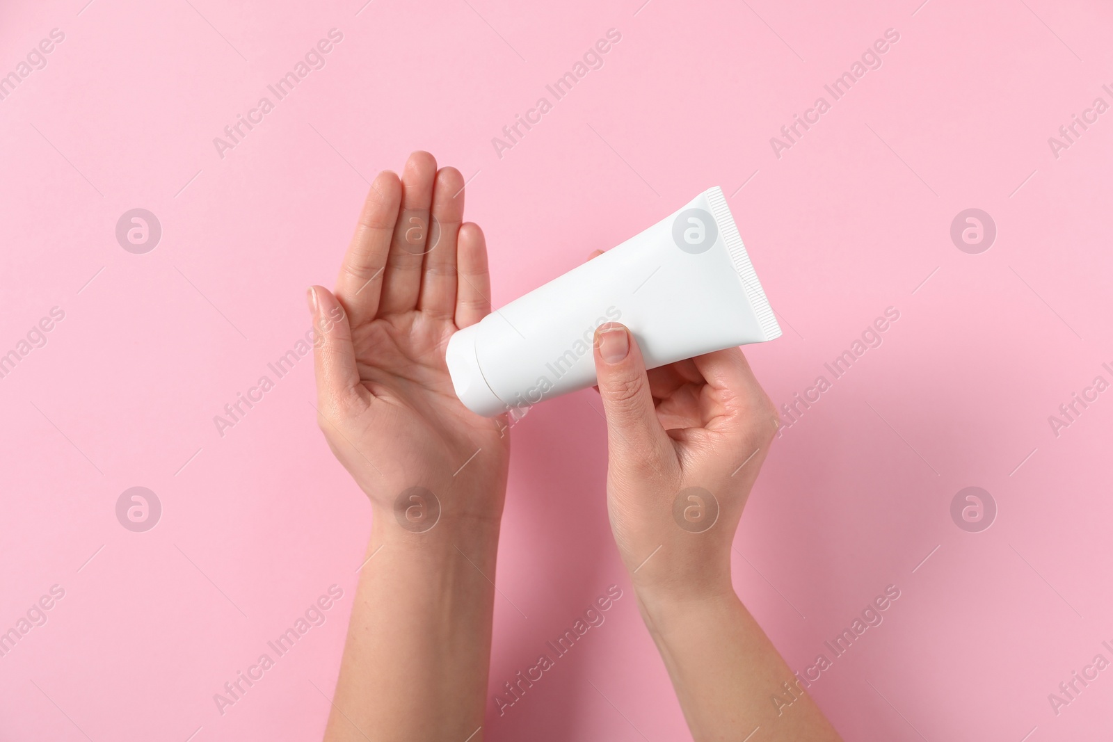 Photo of Woman with tube of hand cream on pink background, top view