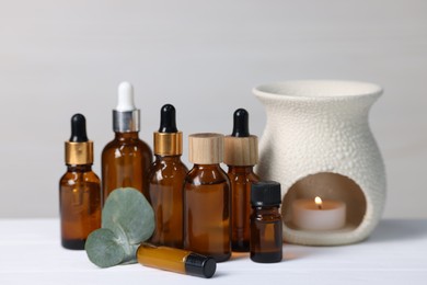 Photo of Different aromatherapy products, burning candle and eucalyptus leaves on white wooden table against light background