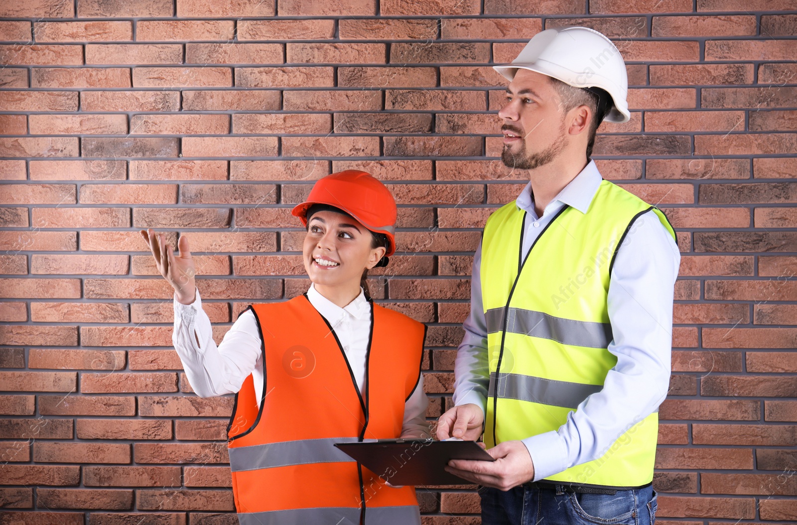 Photo of Industrial engineers in uniforms with clipboard on brick wall background. Safety equipment