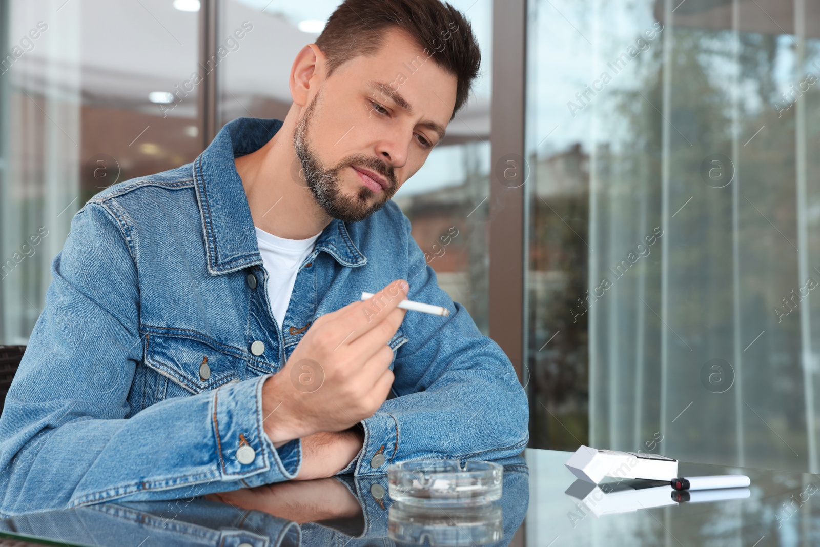 Photo of Handsome man smoking cigarette at table in outdoor cafe