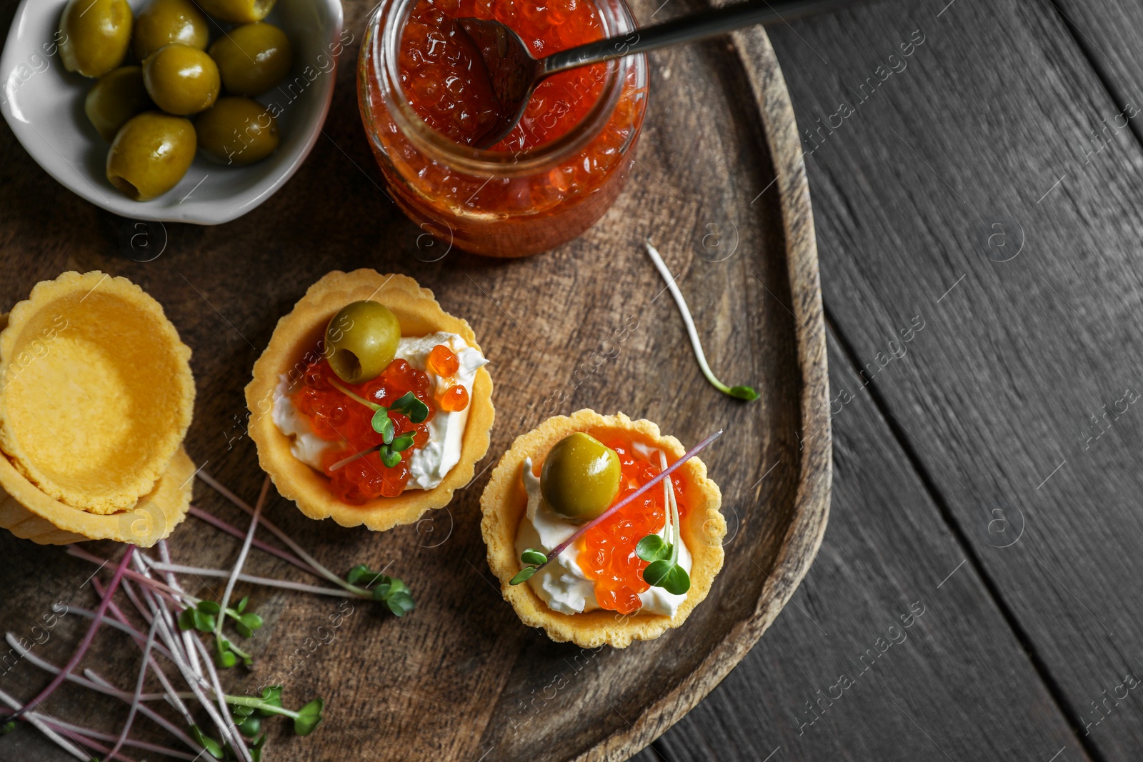 Photo of Delicious tartlets with red caviar and cream cheese served on wooden table, flat lay. Space for text