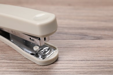 Photo of Beige stapler with staples on wooden table, closeup. Space for text