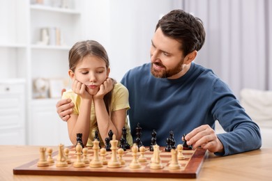 Photo of Father teaching his daughter to play chess at home