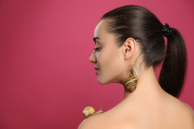 Beautiful young woman with snails on her body against pink background. Space for text