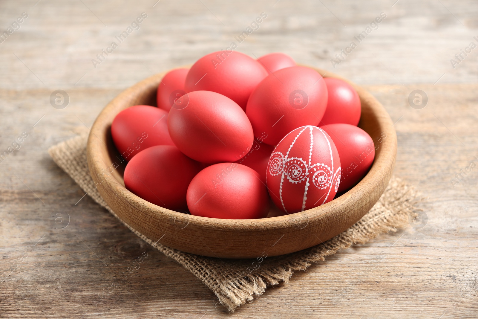 Photo of Wooden bowl with red painted Easter eggs on table