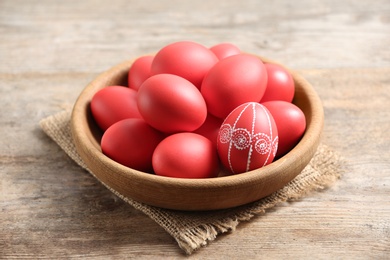 Wooden bowl with red painted Easter eggs on table