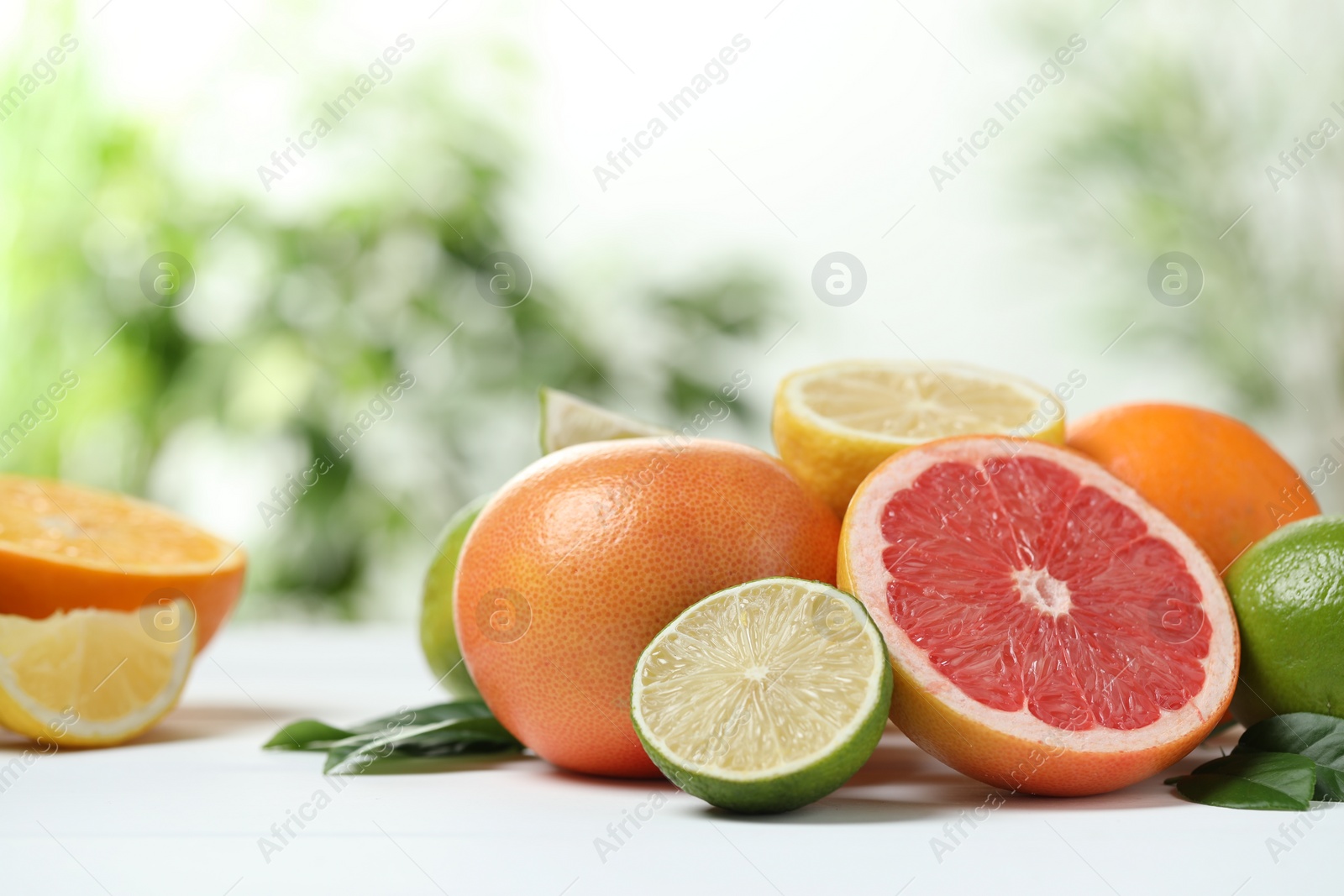 Photo of Different fresh citrus fruits and leaves on white table against blurred background, closeup