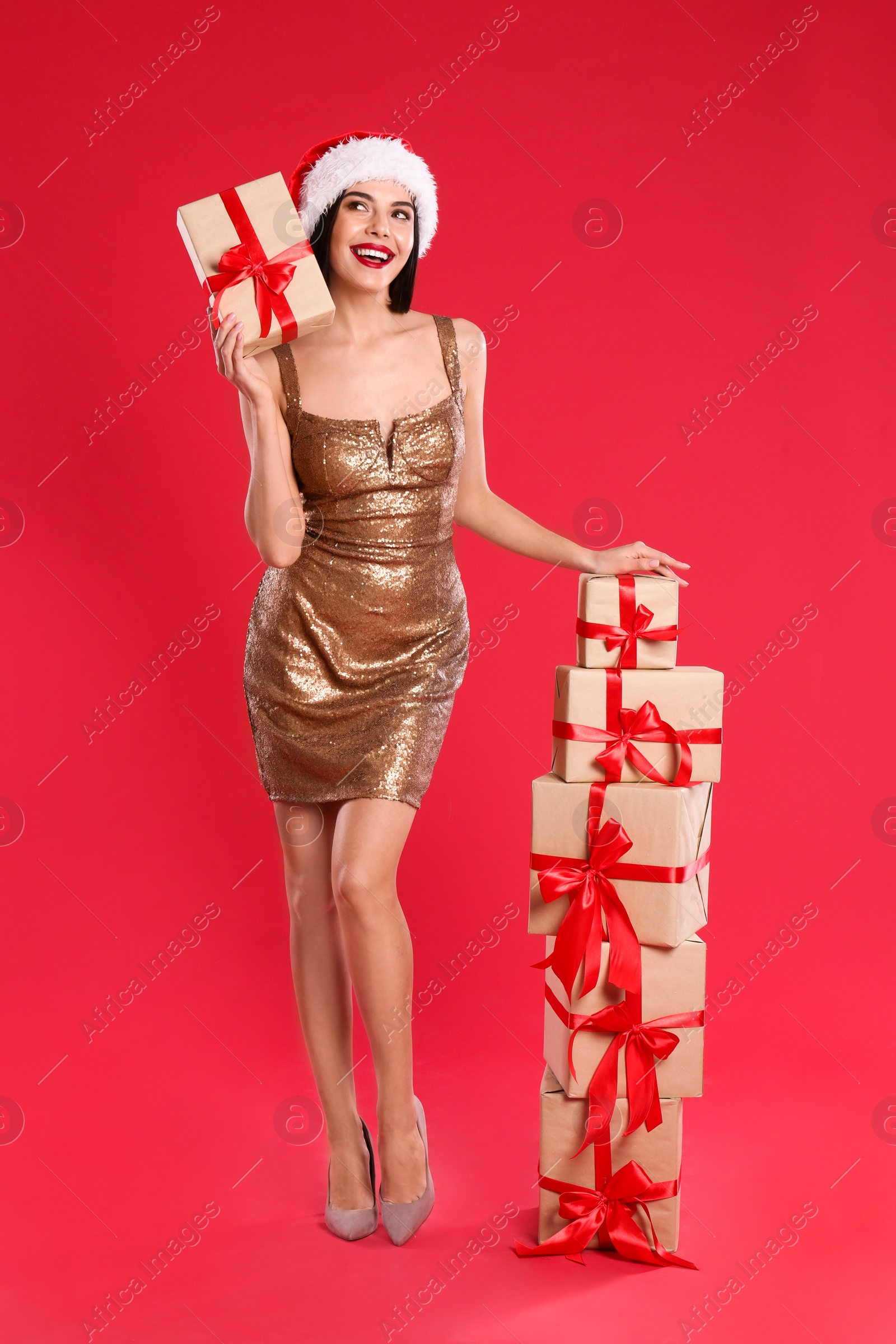 Photo of Woman in golden dress and Santa hat with Christmas gifts on red background