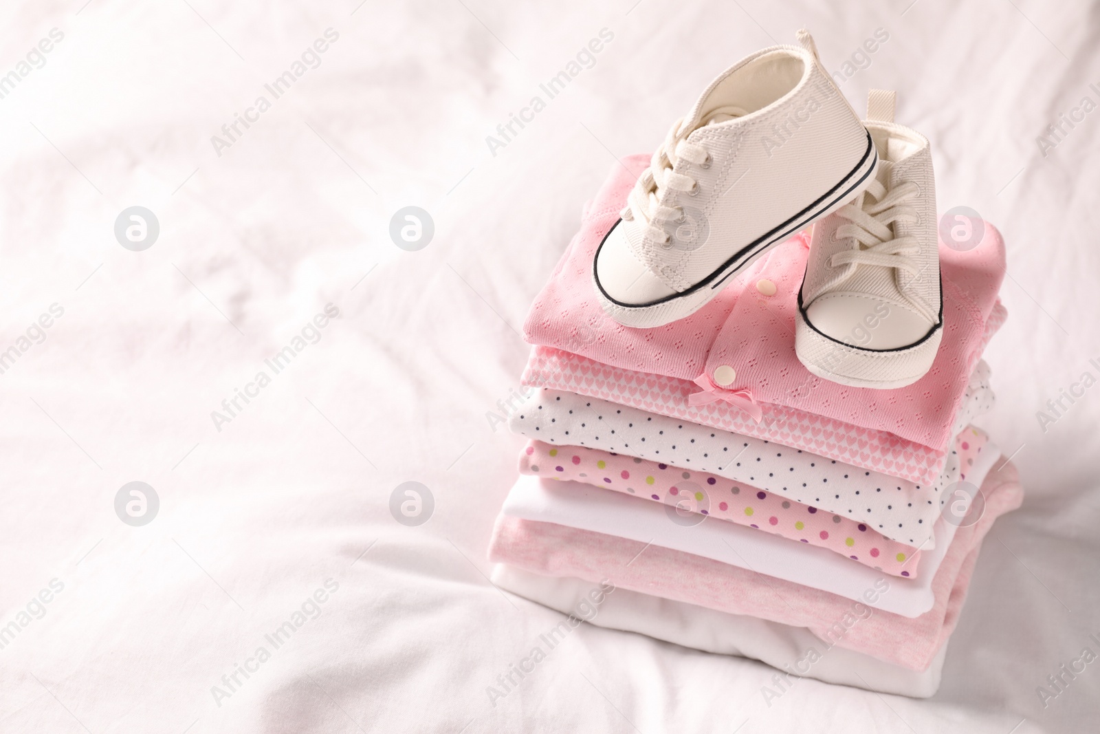 Photo of Stack of baby girl's clothes and shoes on bed. Space for text