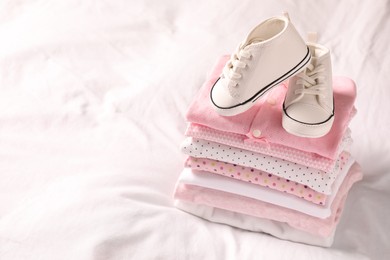 Photo of Stack of baby girl's clothes and shoes on bed. Space for text