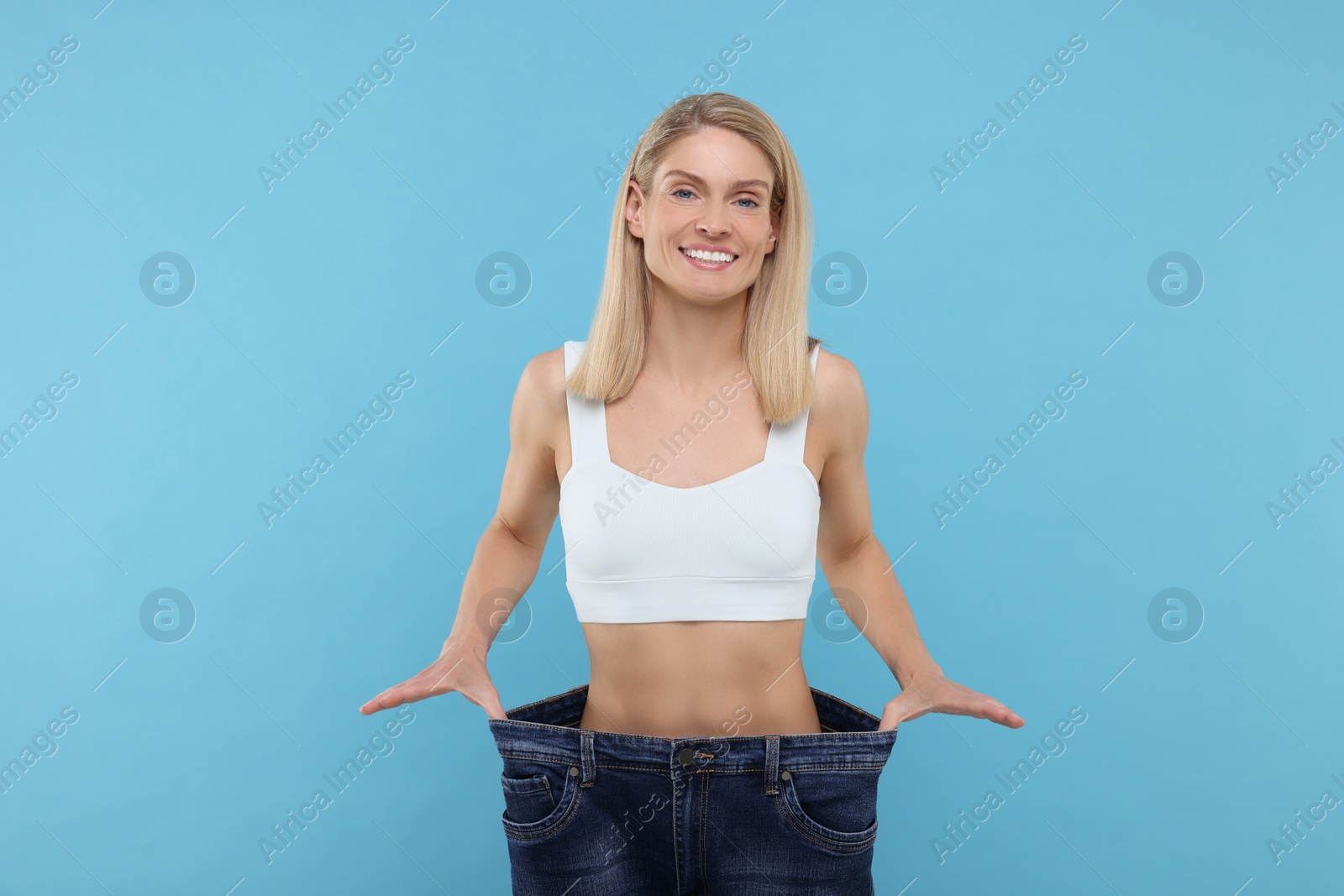 Photo of Slim woman wearing big jeans on light blue background. Weight loss
