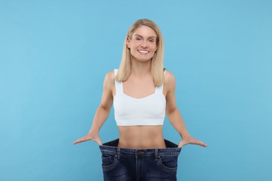 Photo of Slim woman wearing big jeans on light blue background. Weight loss