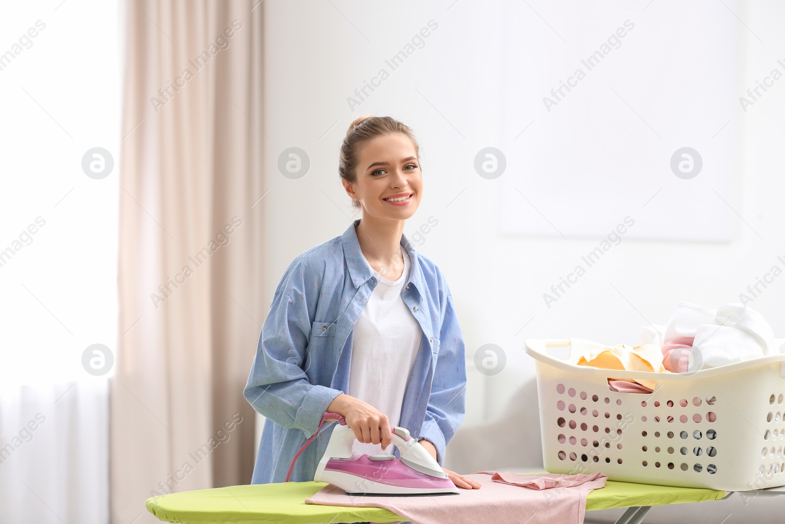 Photo of Young pretty woman ironing clean laundry indoors