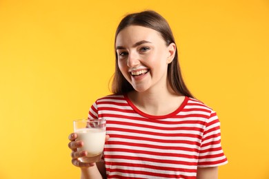 Happy woman with milk mustache holding glass of tasty dairy drink on orange background