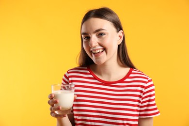 Photo of Happy woman with milk mustache holding glass of tasty dairy drink on orange background