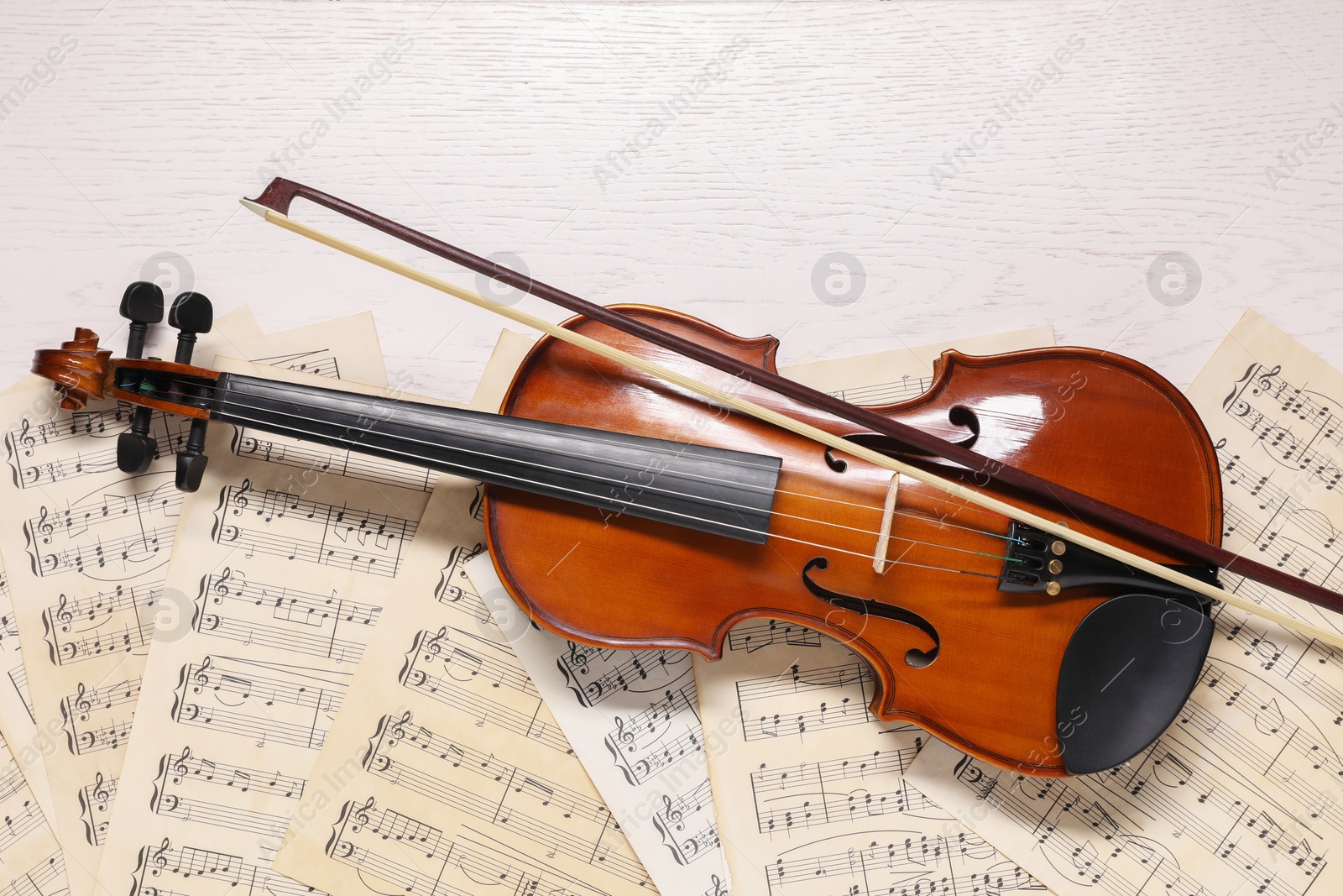 Photo of Violin, bow and music sheets on white wooden table, top view