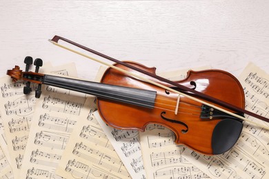 Photo of Violin, bow and music sheets on white wooden table, top view