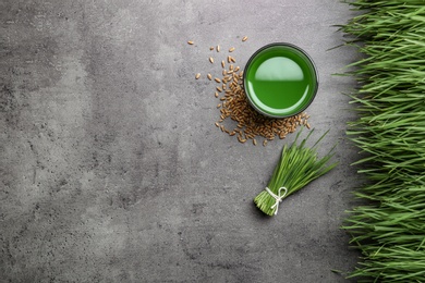 Photo of Flat lay composition with glass of wheat grass juice on grey stone background. Space for text