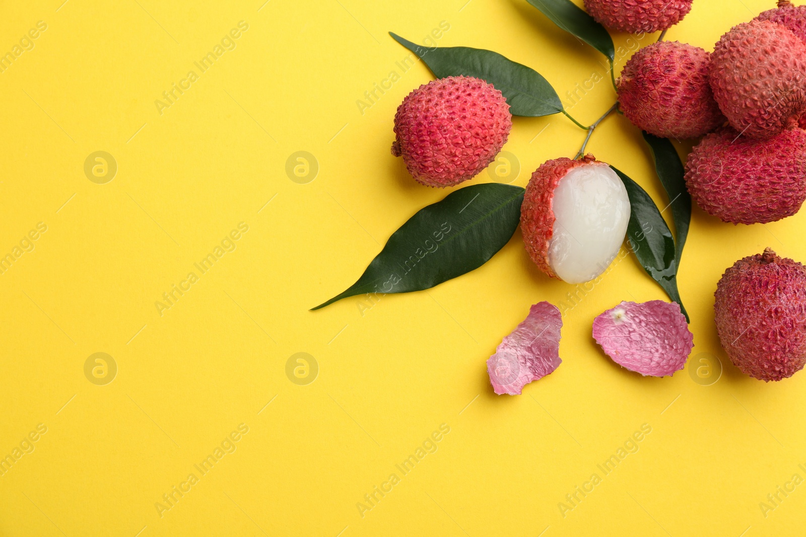 Photo of Fresh ripe lychees with leaves on yellow background, flat lay. Space for text