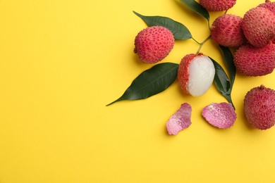 Photo of Fresh ripe lychees with leaves on yellow background, flat lay. Space for text