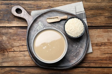 Tasty sesame paste and seeds on wooden table, top view