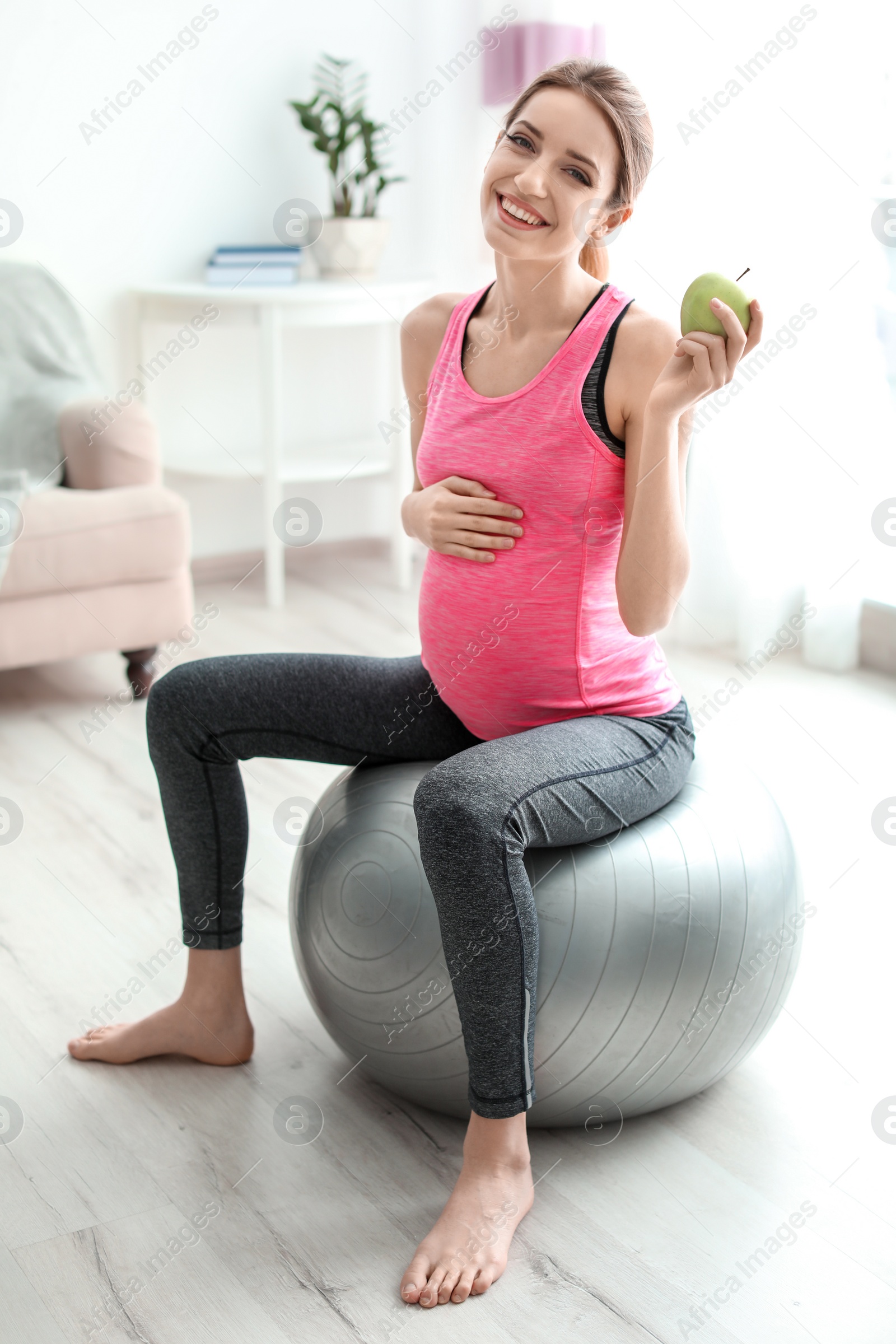 Photo of Young pregnant woman holding apple at home