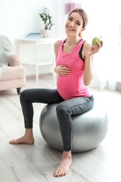 Young pregnant woman holding apple at home