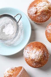 Delicious sweet muffins, plate and sieve on white marble table, flat lay