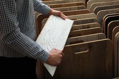 Photo of Man with sample of light wooden flooring in shop, closeup