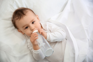 Photo of Cute little baby with bottle lying in comfortable crib, top view. Bedtime