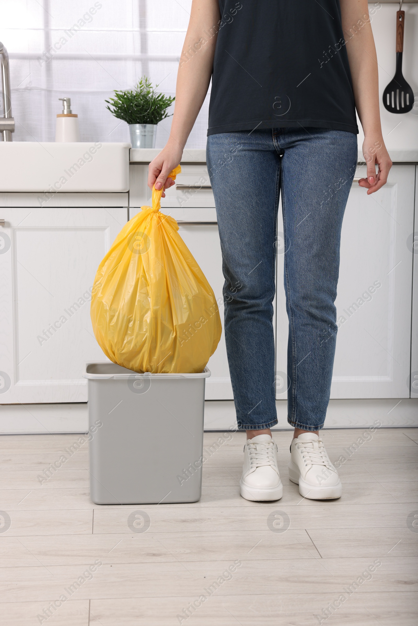 Photo of Woman taking garbage bag out of trash bin in kitchen, closeup