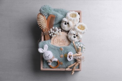 Photo of Wooden box with baby clothes, booties and accessories on grey background, top view