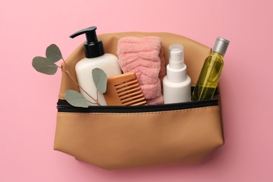 Photo of Preparation for spa. Compact toiletry bag with different cosmetic products and eucalyptus on pink background, top view