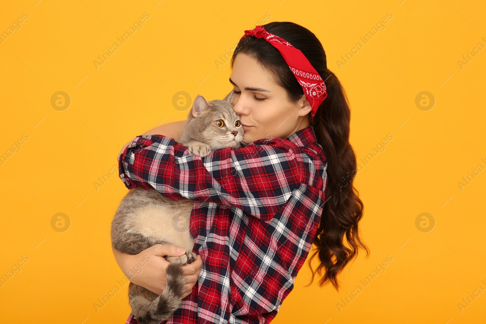 Photo of Young woman kissing her adorable cat on yellow background