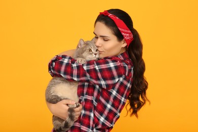 Photo of Young woman kissing her adorable cat on yellow background