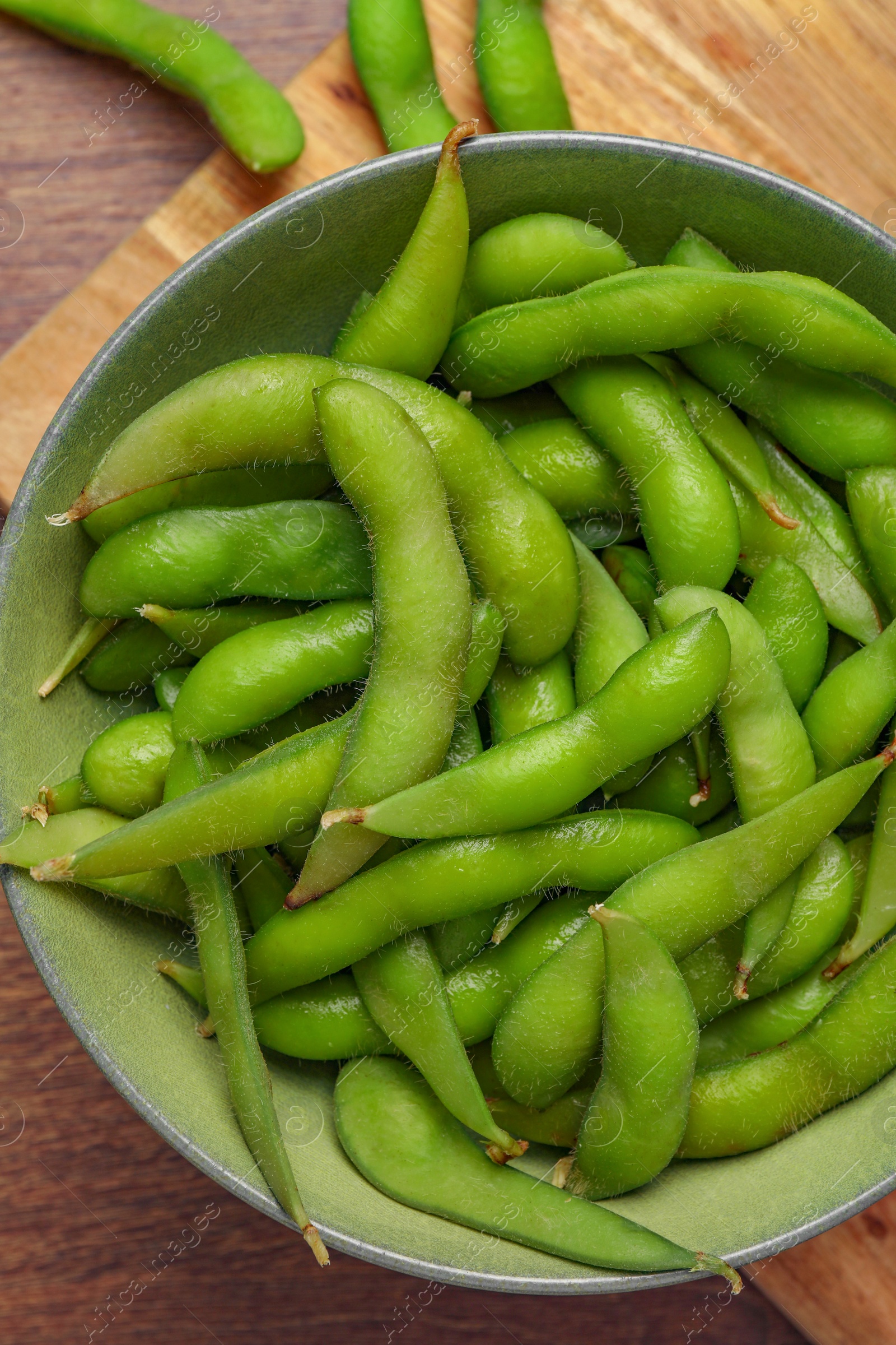 Photo of Bowl with green edamame beans in pods on wooden table, top view