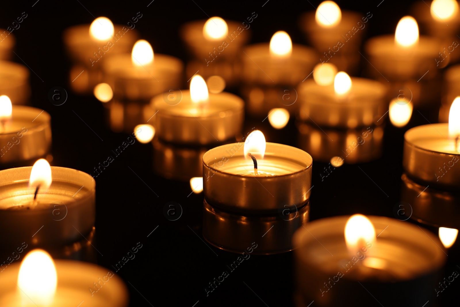 Photo of Burning candles on mirror surface in darkness, closeup
