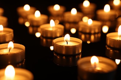 Burning candles on mirror surface in darkness, closeup