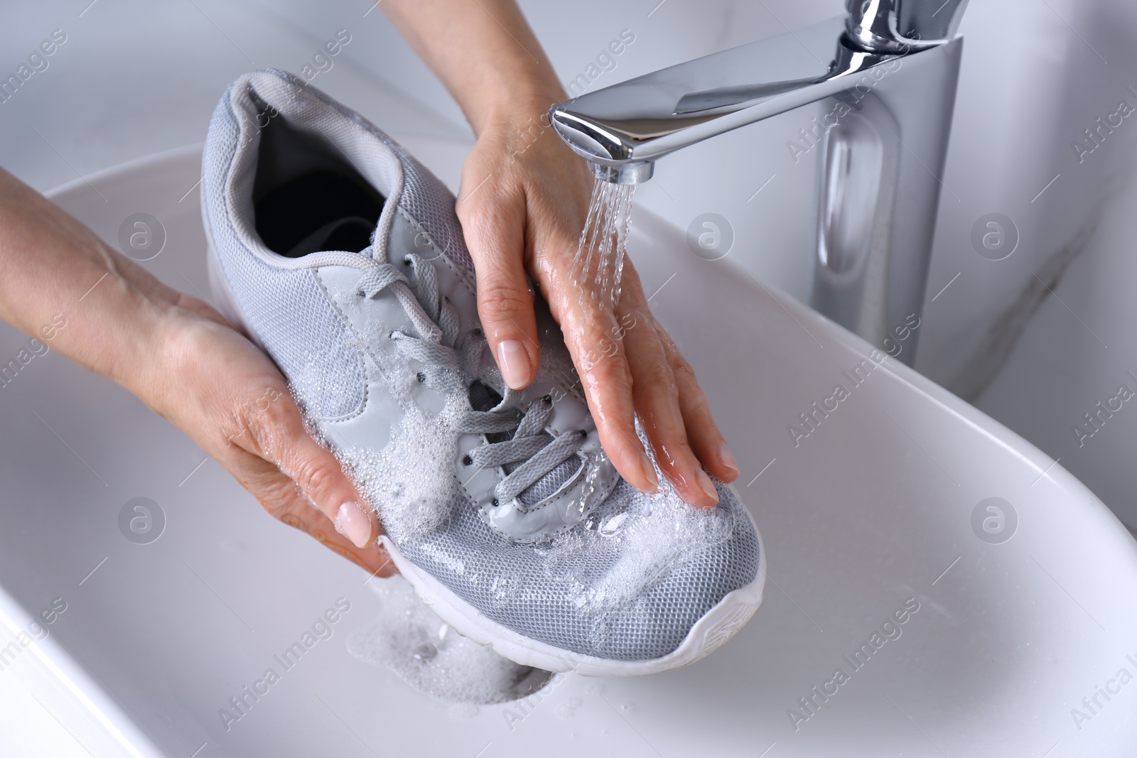 Photo of Woman washing sport shoe in sink, closeup