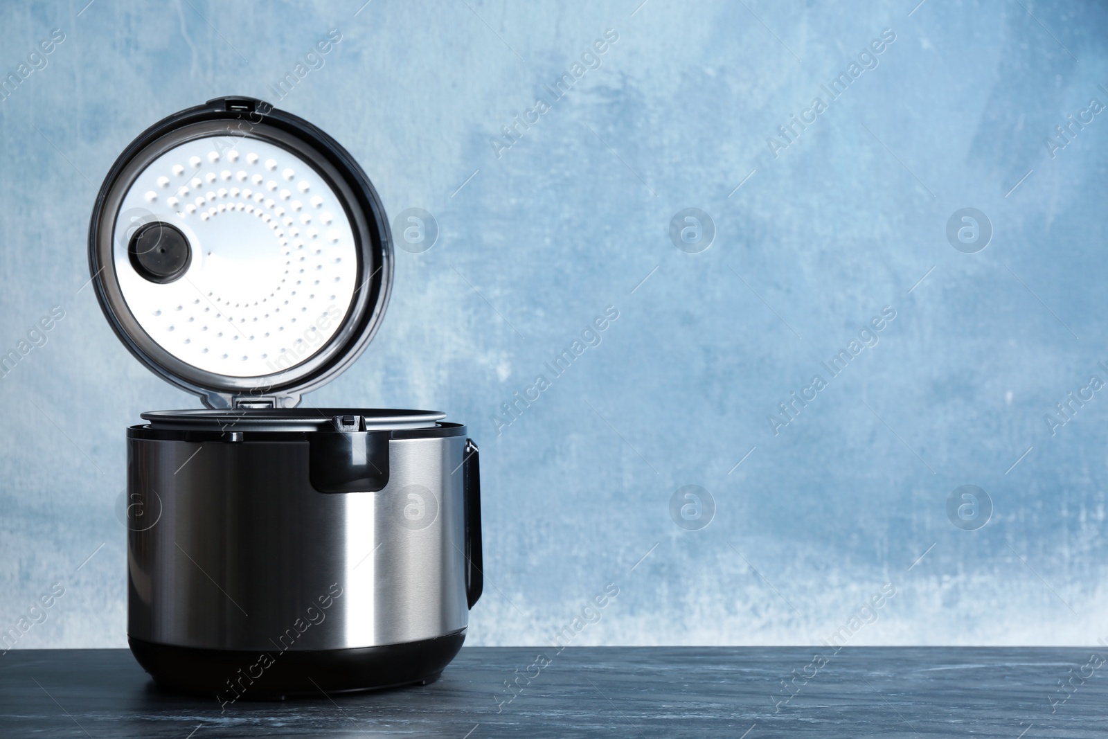 Photo of Modern powerful multi cooker on table against color background. Space for text